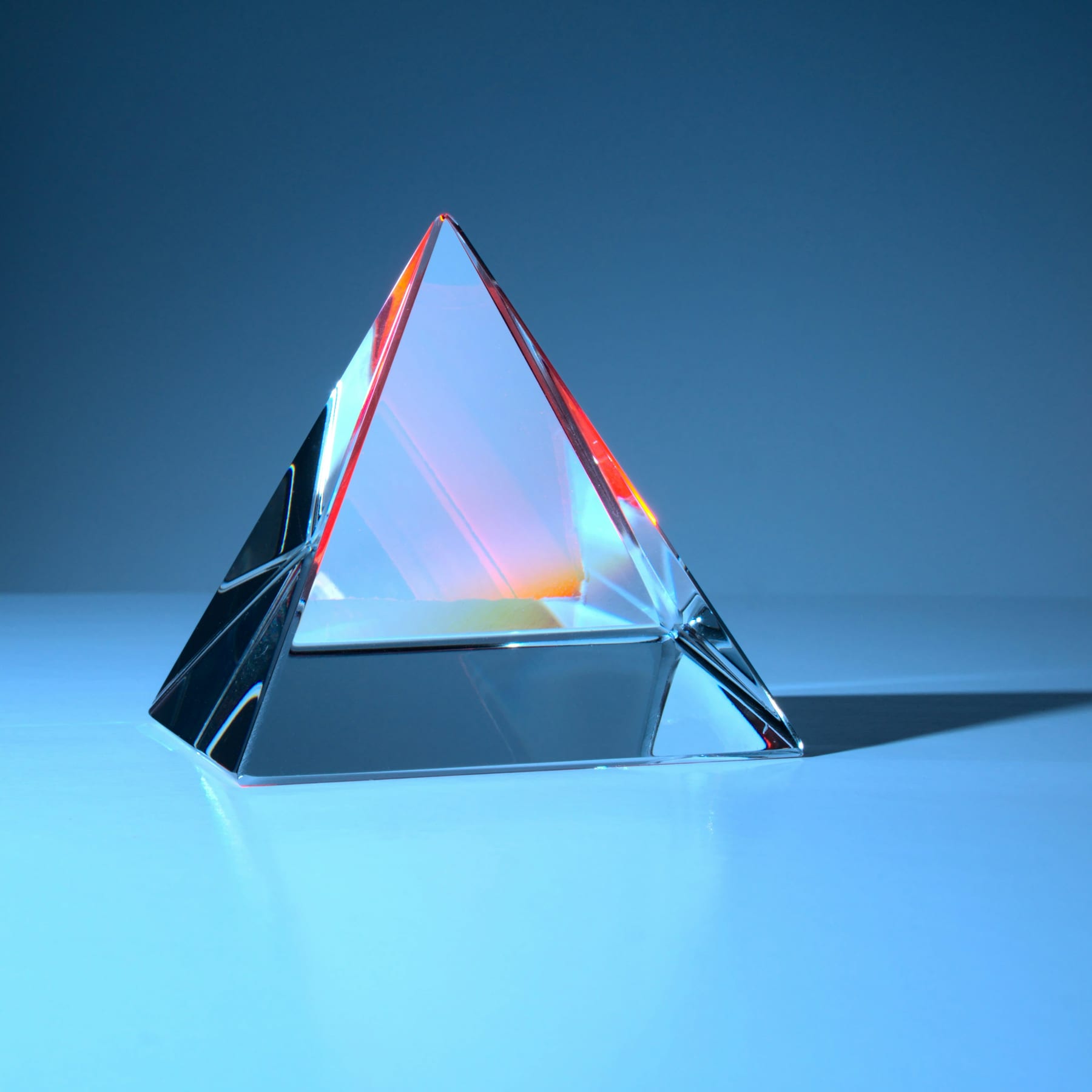 A solid glass prism standing on a lit surface, its edges catching colour
